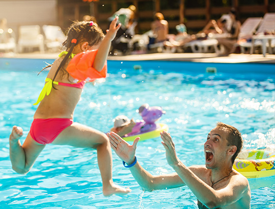 Girl jumping into pool into parents arms