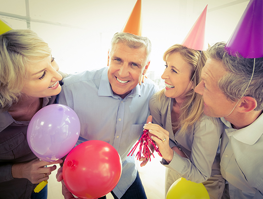 Group of adults holding balloons and wearing party hats