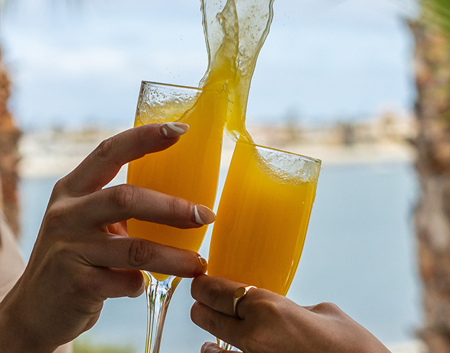 Two hands holding mimosas making a toast
