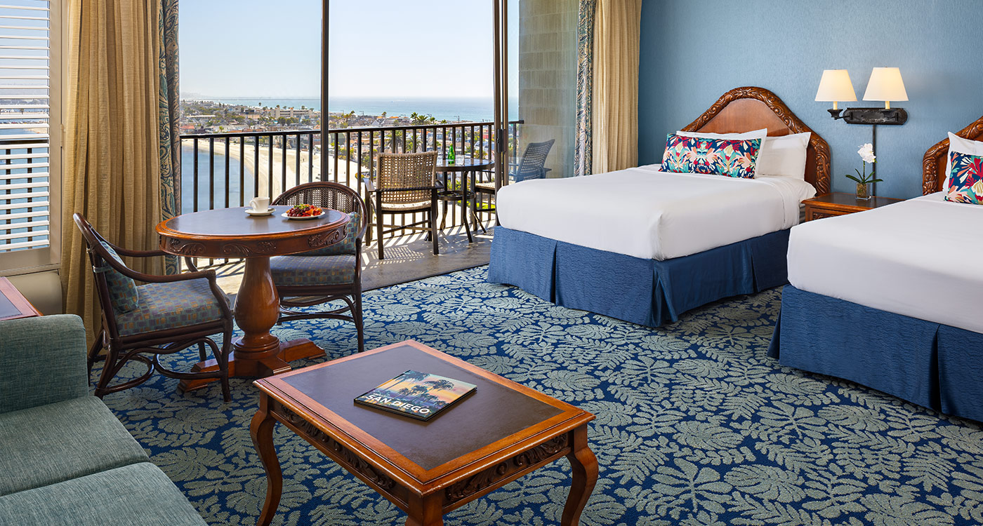 A hotel room with two beds, a sofa, a coffee table, and a balcony with an ocean view.