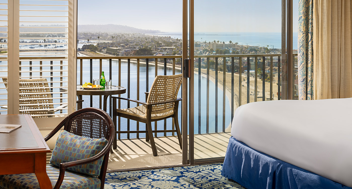 A hotel room with a bed, chair, and table on the balcony overlooking the ocean.