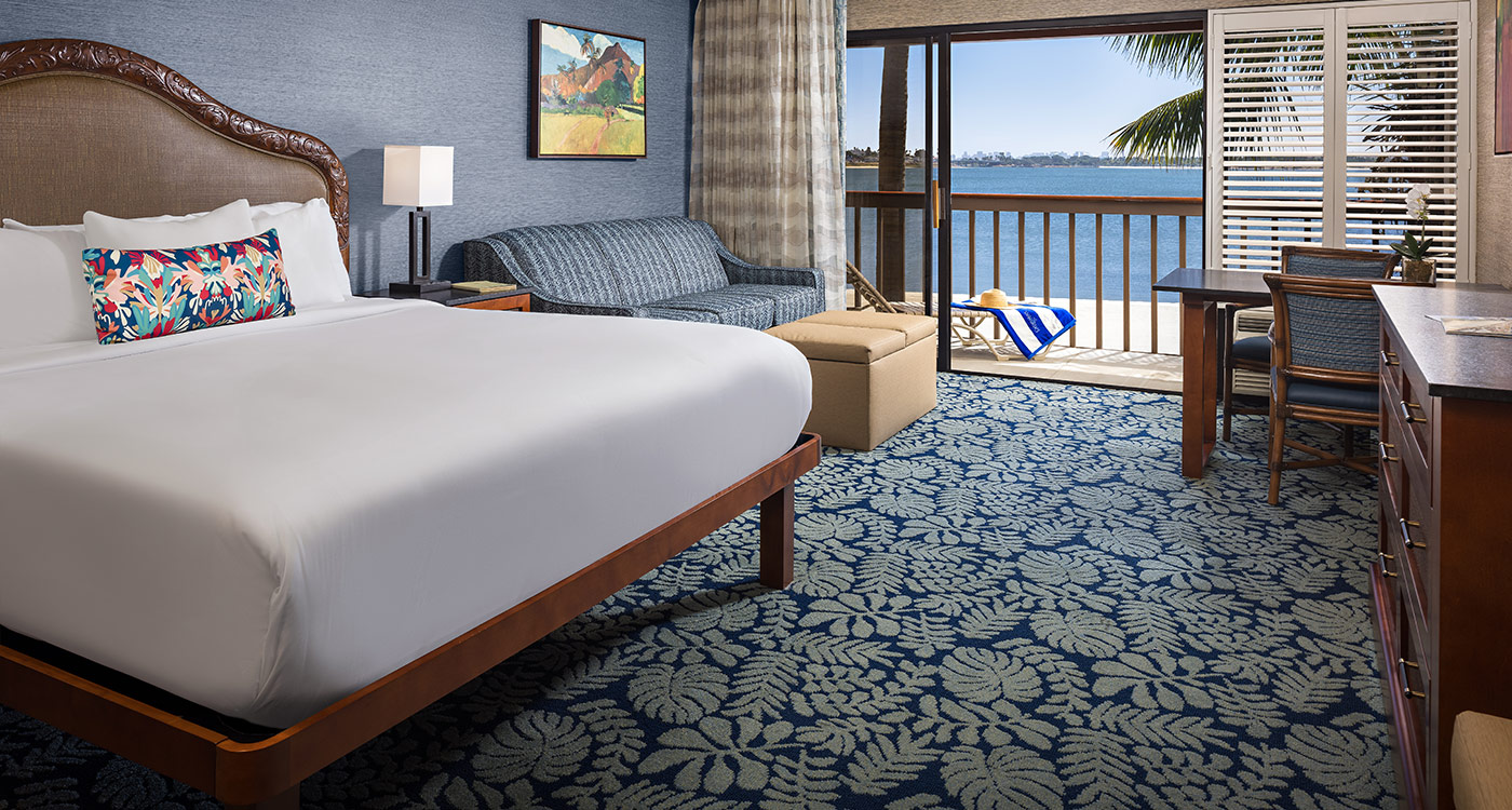 A hotel room with a large bed, desk, sofa, and balcony with a view.