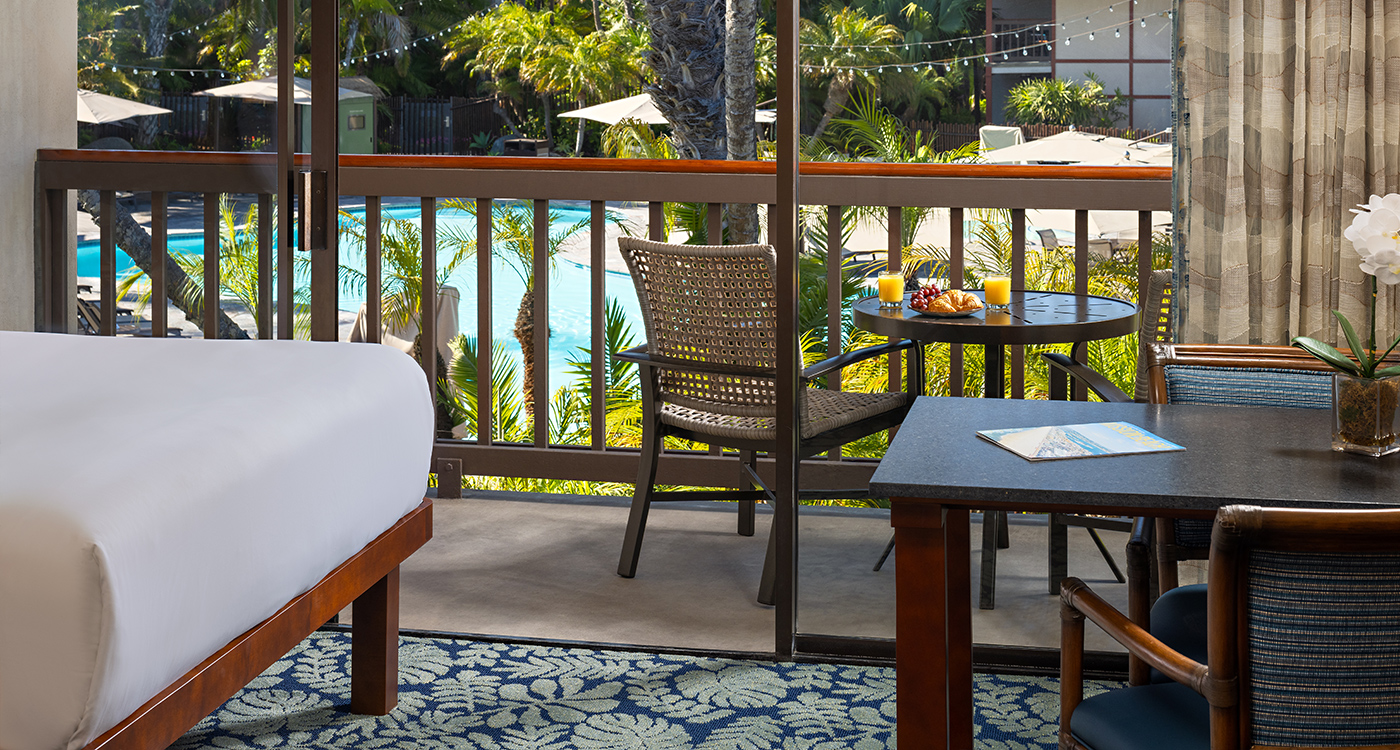A hotel room with a bed, table, and chairs on the balcony overlooking the pool.
