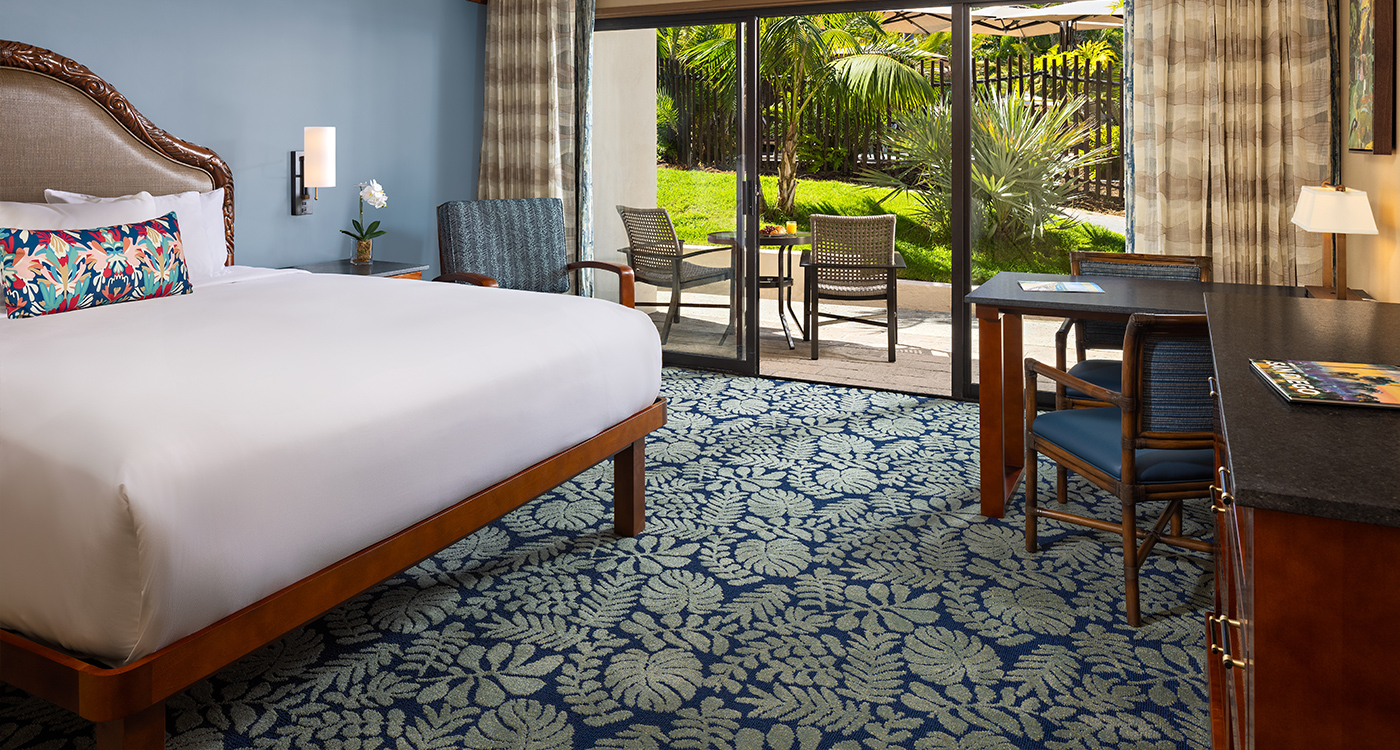 A hotel room with a bed, desk, chair, and door leading to a balcony