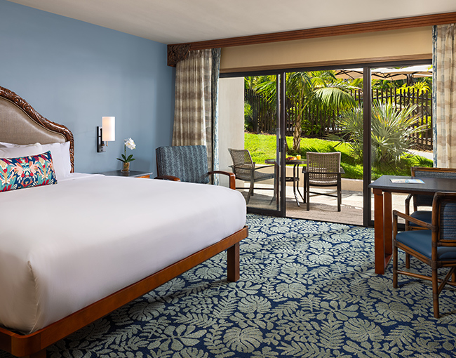 A hotel room with a large bed, sliding glass doors leading to a patio, and a desk.
