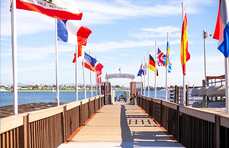 A pier with flags on either side leading to a body of water under a blue sky.
