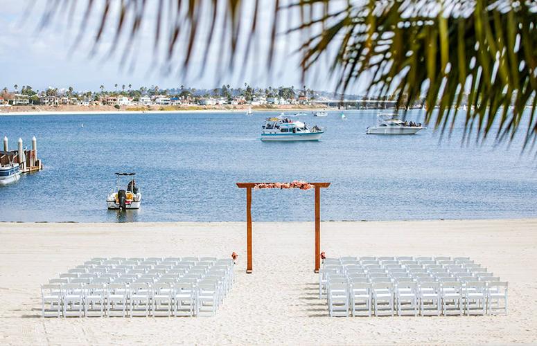 A beach setup for a wedding with a wooden arch, white chairs, and a serene ocean view.