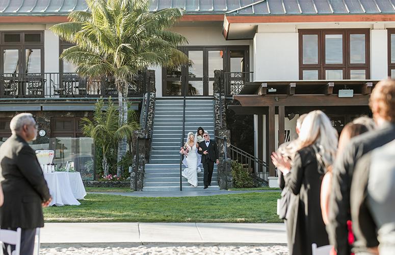 The bride making a grand entrance as she walks down the staircase to the beach at the Catamaran Resort Hotel.