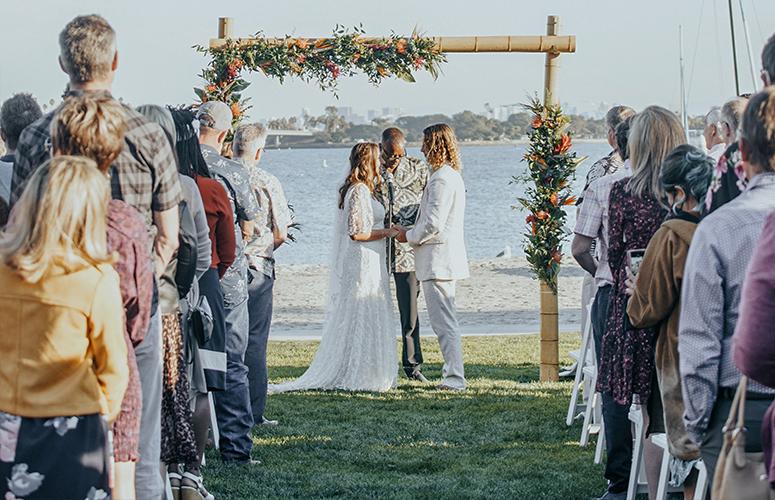 A wedding ceremony on a beach with a floral arch