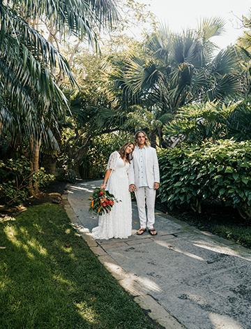 The bride and groom pose for a photo in the lush tropical gardens at their wedding at the Catamaran Resort Hotel with an exotic bouquet of flowers at her side.